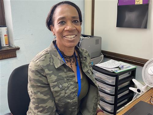 Teacher wearing a green top with necklace and smiling..